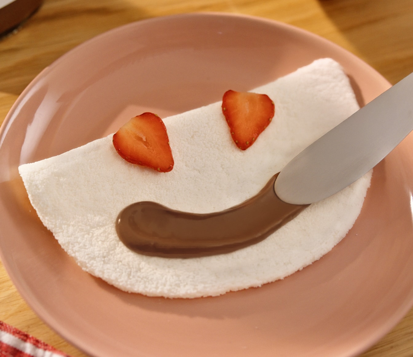 Crepe sobre um prato branco, decorado com Nutella, banana e blueberries com o formato de um rosto sorrindo.