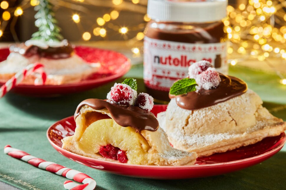 Koláč z rozpolených jabĺk na červenom tanieri, Nutella® a vianočná výzdoba v pozadí.