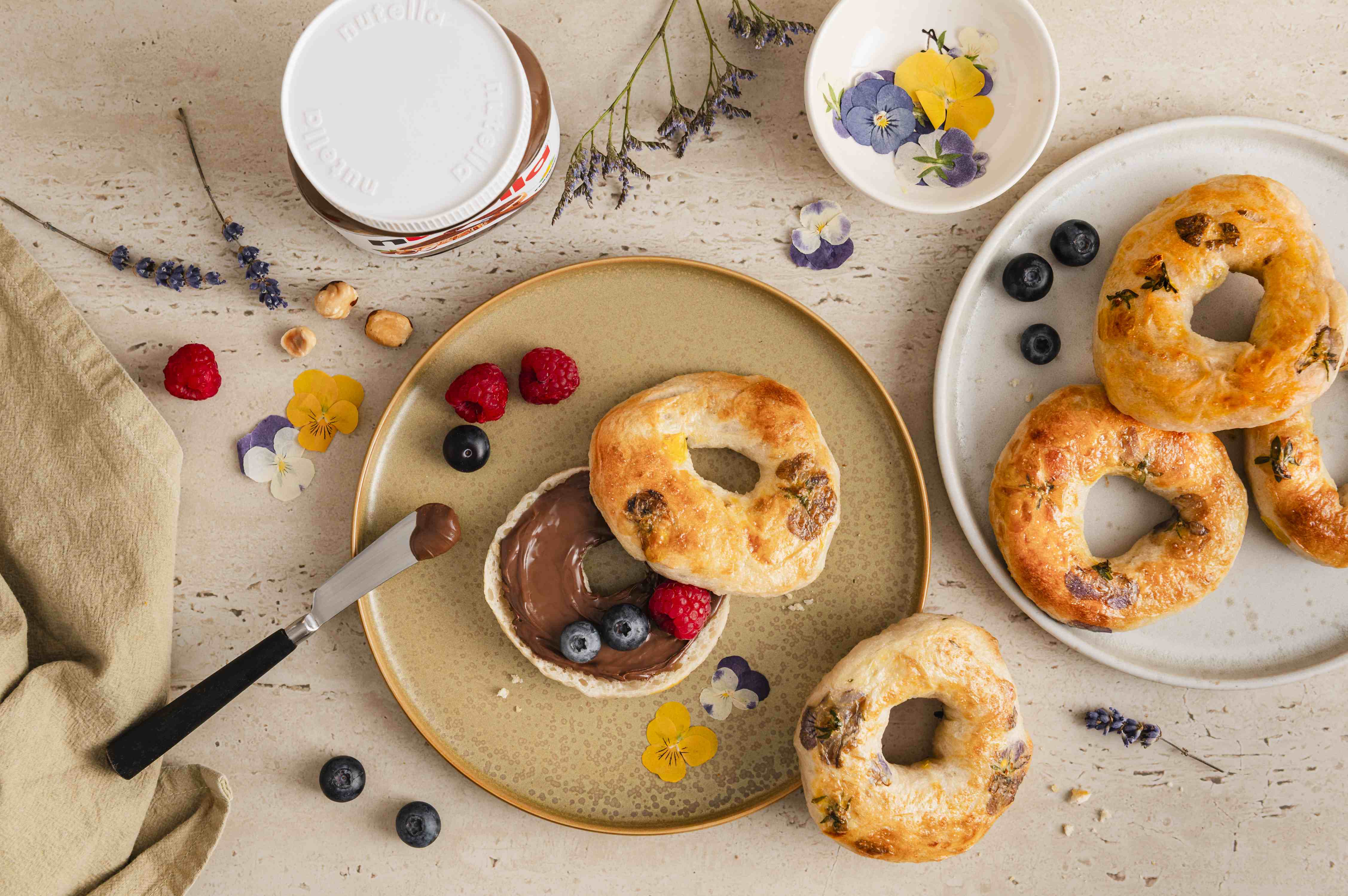 Runder Bagel mit essbaren Blüten, bestrichen mit nutella, garniert mit Himbeeren und Blaubeeren