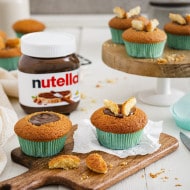 Zarte Vanille-Cupcakes mit Nutella-Frosting, Schokoladenstückchen und Nusskrokant auf Teller.