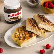 Luftige Focaccia-Stücke mit nutella®-Topping auf einem Teller, daneben Himbeeren und ein Glas nutella®