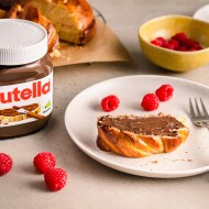 Scheibe Beeren-Babka-Hefezopf mit nutella® bestrichen, serviert auf einem Teller mit Himbeeren		