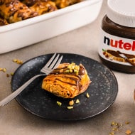 Nutella-Glas dekorativ mit Früchten, Löffel und Leinenserviette daneben arrangiert.