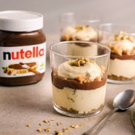 Nutella auf Toast gezeigt, Aufstrich glänzend, Glas im unscharfen Hintergrund.