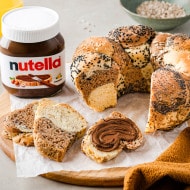 Bereinigtes Foto: Nutella Glas neben frisch gebackenem Gebäck auf Holz.