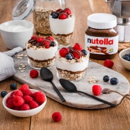 Joghurt mit Müsli, Nutella-Swirl und frischen Früchten, serviert in Schale.