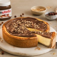 Gebackener Käsekuchen mit nutella® und Nüssen, ein Stück wird serviert. Dazu gibt es nutella®, Orangen und Nüsse.