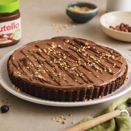 Kuchen mit nutella® Plant-Based und Nüssen garniert; daneben ein Glas nutella® Plant-Based, Blaubeeren und weitere Nüsse 
