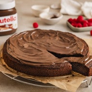 Ein Schokoladenkuchen mit nutella®-Glasur, ein Stück davon abgeschnitten und mit Himbeeren bestreut, daneben ein nutella®-Glas.