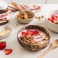 Rosarote Beeren-Smoothie-Bowls mit Erdbeeren, Bananen und Nutella-Topping auf hellem Hintergrund.