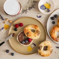 Runder Bagel mit essbaren Blüten, bestrichen mit nutella, garniert mit Himbeeren und Blaubeeren