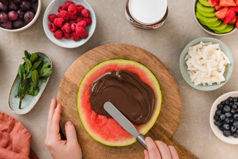 Nutella-Glas auf rustikalem Brett, begleitet von Haselnüssen und dekorativem Löffel.