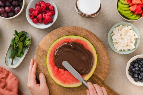 Nutella-Glas auf rustikalem Brett, begleitet von Haselnüssen und dekorativem Löffel.