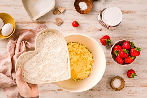 Zutaten für Herz Cookies mit Nutella®, darunter Mehl, Butter, Zucker und Erdbeeren, auf einer Küchenoberfläche arrangiert.