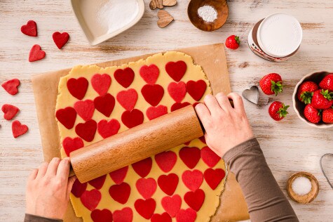 Der Teig wird mit herzförmigen Ausstechern in roten und rosa Herzen auf einer bemehlten Oberfläche ausgestochen.