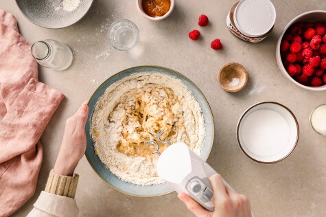 Zutaten für Babka-Teig mit Mehl, Zucker und Hefe werden in einer Schüssel mit dem Handrührgerät vermengt, daneben Himbeeren und nutella®		