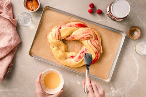 Ungebackener Babka-Zopf mit Himbeerfüllung wird auf einem Backblech geformt und mit Eigelb bestrichen		