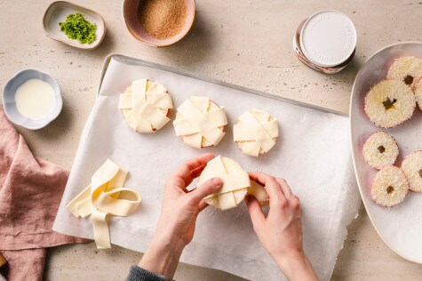 Apfelringe mit Kokospanade werden mit Streifen aus Blätterteig umwickelt
