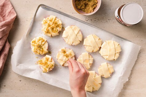 Apfelringe mit Blätterteigstreifen auf Backblech, werden mit Limettenzucker bestreut