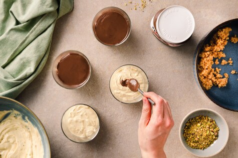 Cheesecake-Creme wird in Gläser gefüllt, darauf wird eine Schicht nutella® gestrichen, daneben Schale mit Pistazien und Keksbröseln