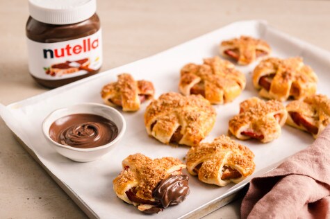 Nahaufnahme: Nutella-Glas mit sichtbaren Haselnussstücken und Löffel auf Brett.