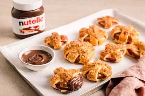 Nahaufnahme: Nutella-Glas mit sichtbaren Haselnussstücken und Löffel auf Brett.