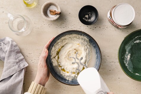 Zutaten für Focaccia-Teig werden mit einem Handrührgerät vermengt, sichtbar sind Mehl, Wasser, Hefe und Olivenöl
