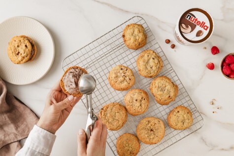 Ein Cookie wird in der linken Hand gehalten, mit der rechten Hand wird eine Kugel nutella Eis platziert. Der Hintergrund zeigt ein Becher nutella Eis.