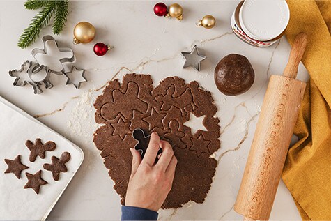 Ausgerollter Lebkuchenteig wird mit Ausstechformen aus Sternen und Tiermotiven verarbeitet. Seitlich liegen ein Nudelholz und ein Glas nutella®.