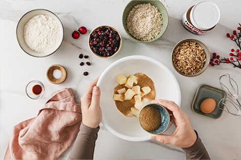 In der Mitte des Fotos liegt eine Schüssel mit Butterwürfeln und braunem Zucker, umgeben von weiteren herrlichen Zutaten.