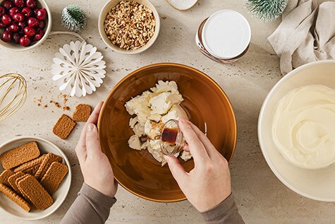 Zu sehen ist eine Schüssel mit Mascarpone und Sahne, in die Vanilleextrakt hinzugeben wird. Drumherum liegen Spekulatius-Kekse und gehackte Haselnüsse.