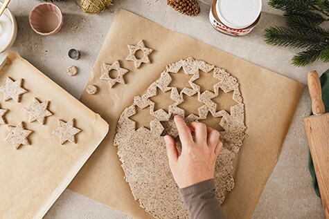 Ein Teig wird mit einem Sternausstecher aus der Masse gestochen und auf ein mit Backpapier bedecktes Blech gelegt.