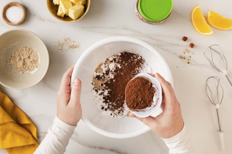 Draufsicht auf Hände, die Kakaopulver in eine Schüssel mit Mehl geben; ein Glas nutella® Plant-Based steht daneben