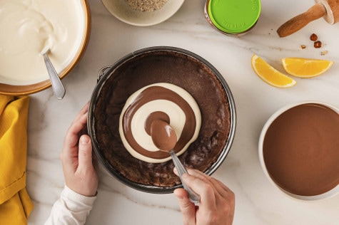 Hände löffeln Schokolade und weiße Sahne in einen Schokoladenboden und formen so einen Wirbel; nutella® Plant-Based steht daneben.