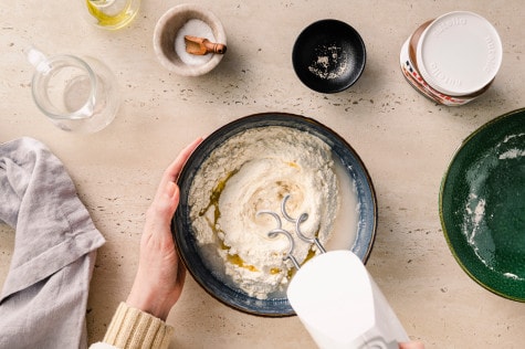 Zutaten für Focaccia-Teig werden mit einem Handrührgerät vermengt, sichtbar sind Mehl, Wasser, Hefe und Olivenöl