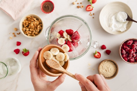 Zubereitung einer Beeren-Smoothie-Bowl mit gefrorenen Früchten im Mixer und Bananenscheiben.