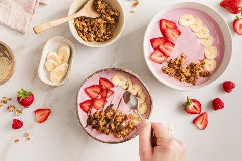 Dekorieren einer rosaroten Smoothie-Bowl mit frischem Obst, Müsli und nsutella von oben fotografiert.