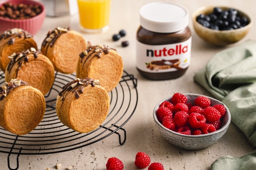 Nutella-Glas neben frisch gebackenem Brot auf rustikalem Holzbrett, serviert.