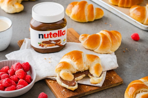 Person streicht Nutella auf Brot in urbaner Küchen- oder Caféumgebung, Nahaufnahme.