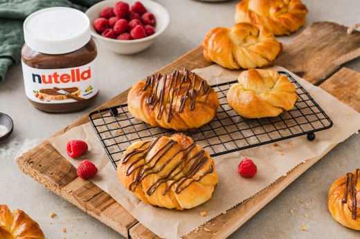 Balkonfrühstück: Nutella-Glas, Croissant und Kaffee in Stadtkulisse am Morgen.