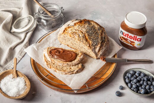 Nutella-Glas begleitet von Gebäck und rustikalem Besteck, einladend arrangiert.