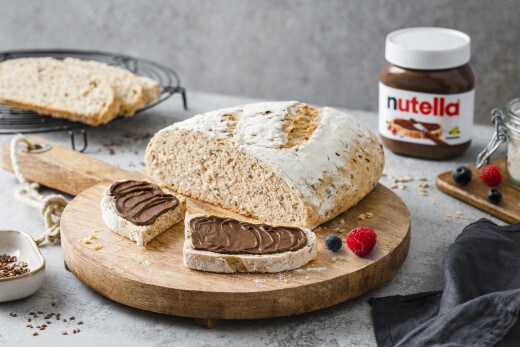 Herobild: Nutella-Glas im Frühstückssetting mit Brot, Früchten und Besteck.