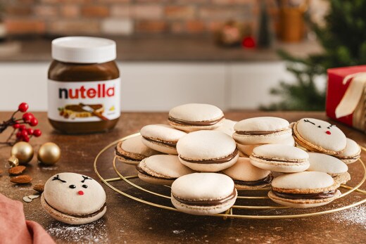Auf einem goldenen Gitter ruhen mehrere fertig gebackene Macarons, die mit nutella® gefüllt sind. Einige Macarons haben eine süße Verzierung.
