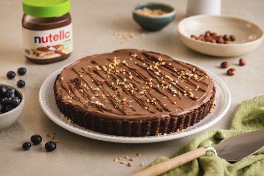 Kuchen mit nutella® Plant-Based und Nüssen garniert; daneben ein Glas nutella® Plant-Based, Blaubeeren und weitere Nüsse 