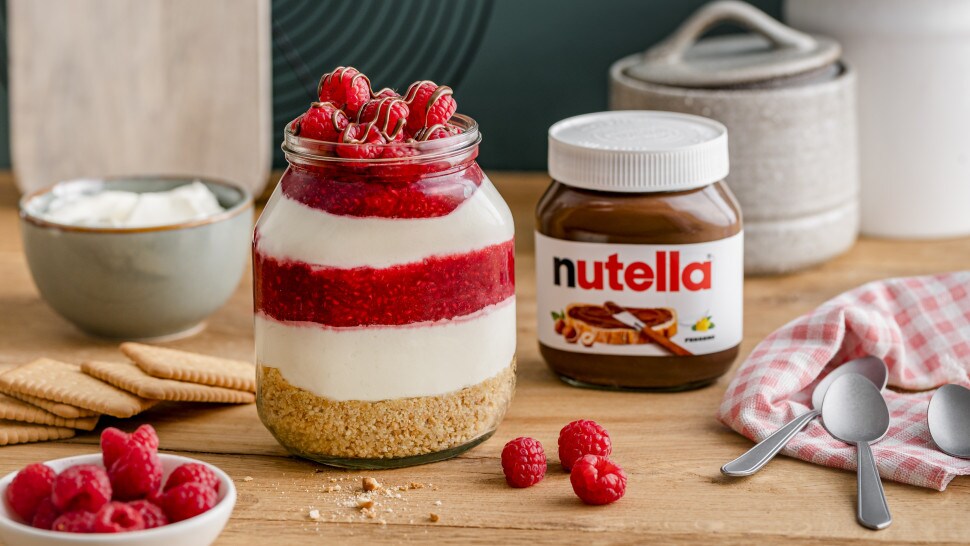 Himbeer-Käsekuchen im Glas mit nutella®, geschichtet mit Keksboden, Creme und Himbeerpüree, dekoriert mit frischen Himbeeren