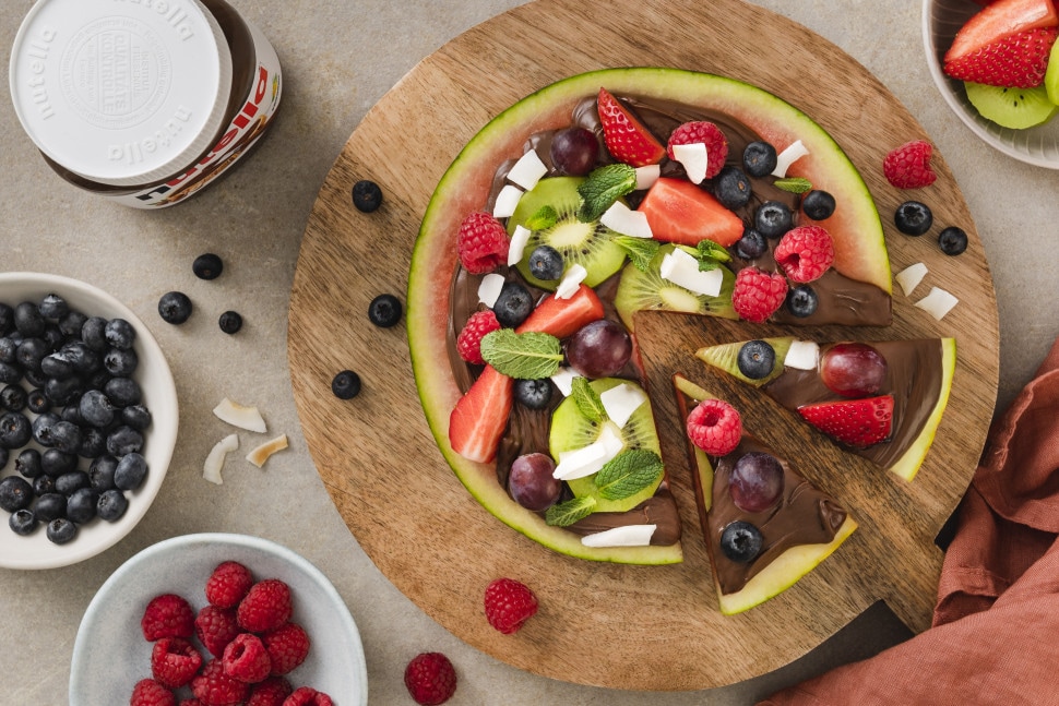 Bunte Wassermelonen-Pizza mit nutella®, belegt mit frischen Früchten wie Erdbeeren, Kiwi, Trauben und Minze