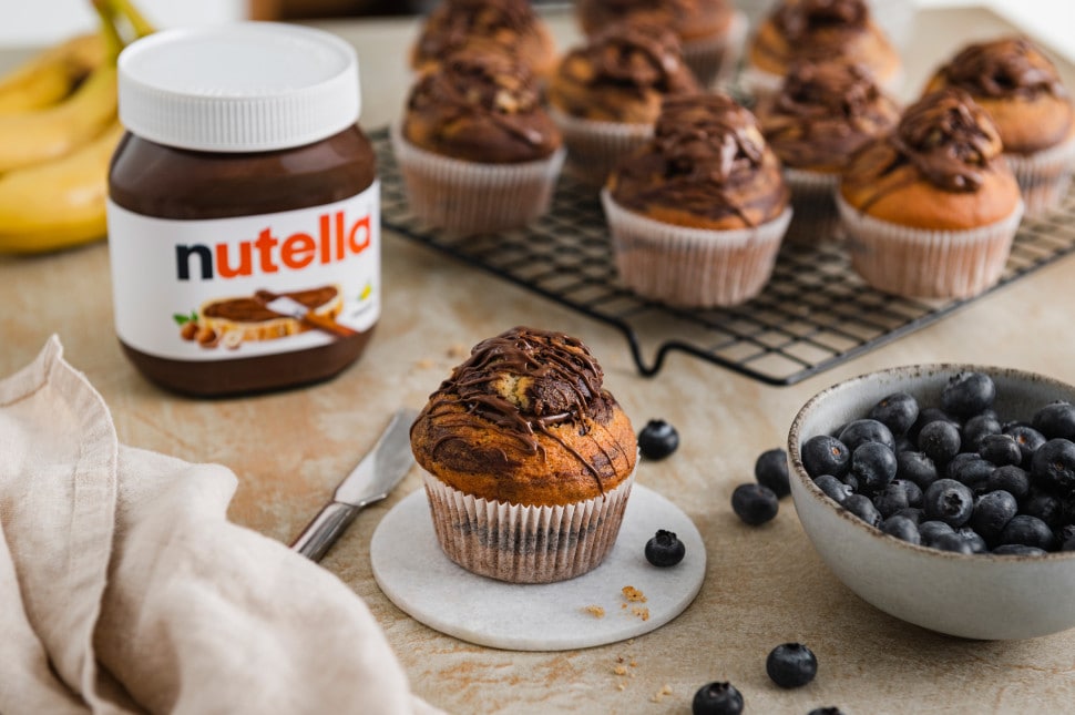 Nahaufnahme: Glas Nutella mit Löffel und Haselnussdekor auf Holzuntergrund.