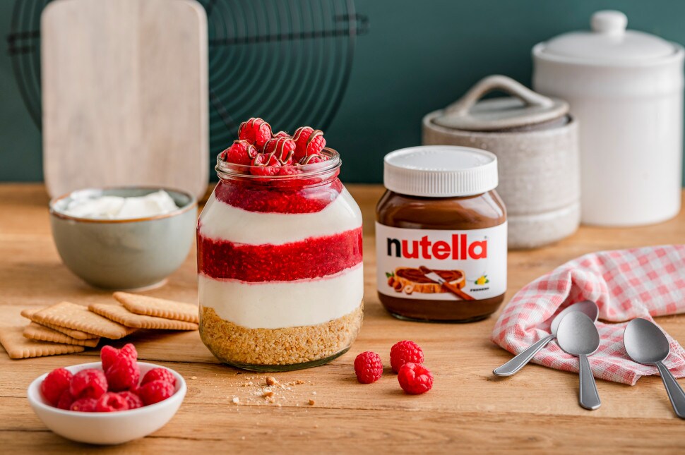 Himbeer-Käsekuchen im Glas mit nutella®, geschichtet mit Keksboden, Creme und Himbeerpüree, dekoriert mit frischen Himbeeren