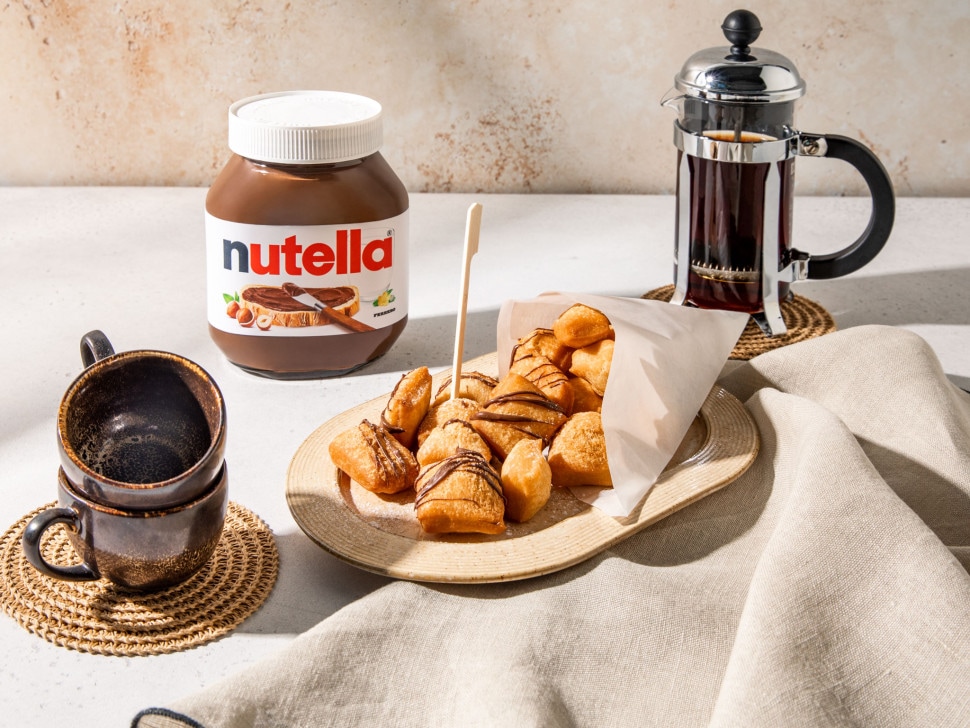 Mandazi-Teigtaschen, goldbraun frittiert, Puderzucker bestäubt und mit Nutella-Dip serviert.