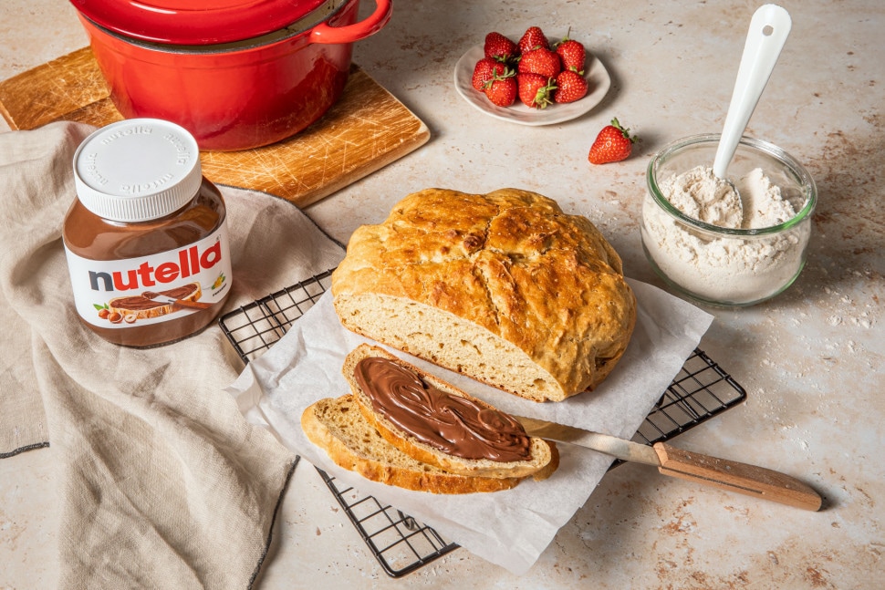 Stimmungsbild: Nutella-Glas neben frisch gebackenem Brot auf rustikalem Holzbrett.